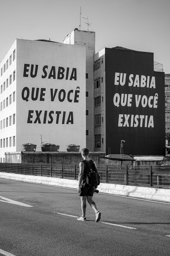 Black and white photo of a city street with bold text on buildings and a pedestrian.